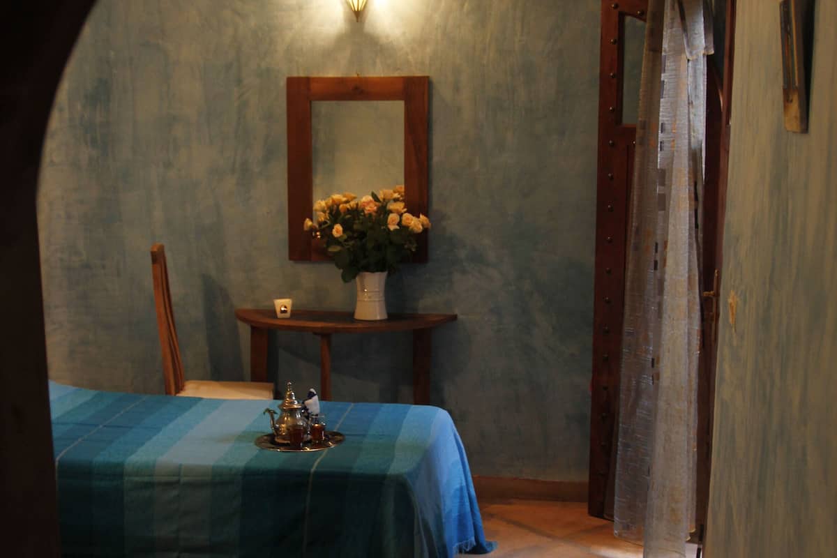 A small, cozy room with two beds, a table with a vase of flowers, and a mirror on the wall.