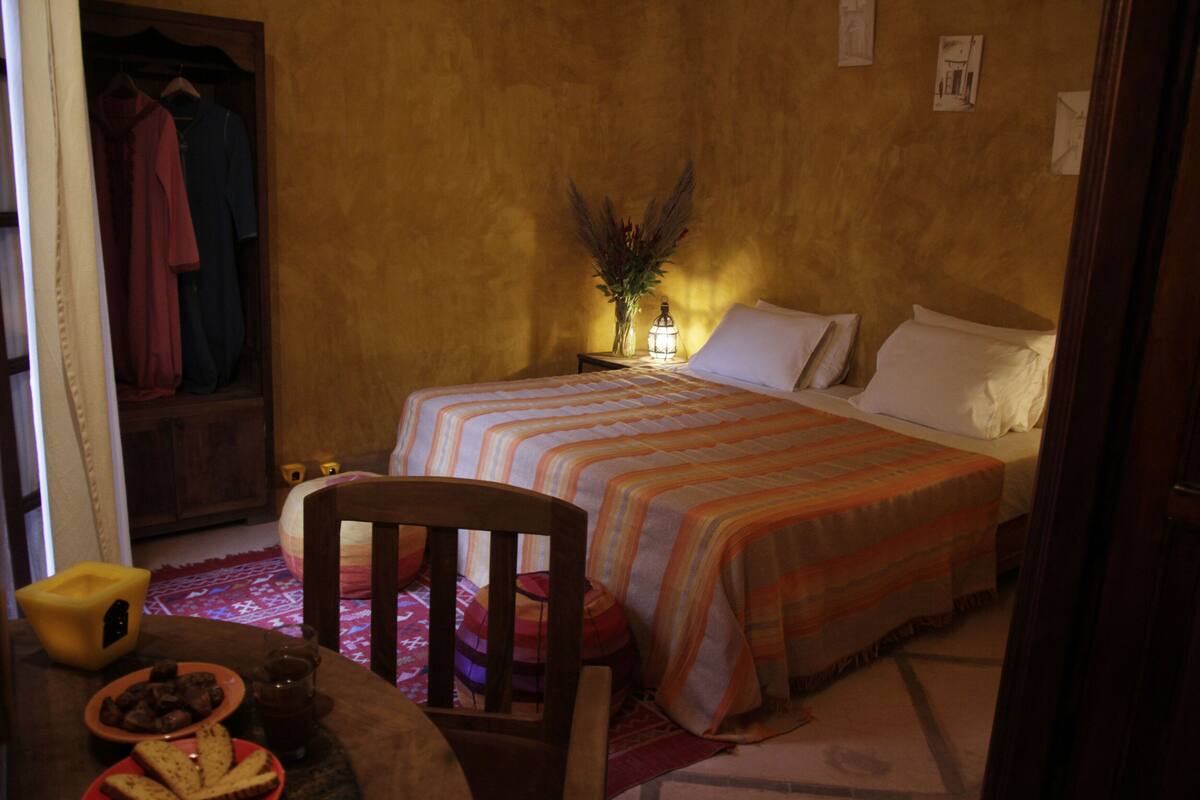 A bedroom with a bed, bedside table, lamp, and a chair.