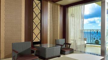 A room with a glass table and two wicker chairs, a large window with a view of the sea, and a sliding door with a patterned design.