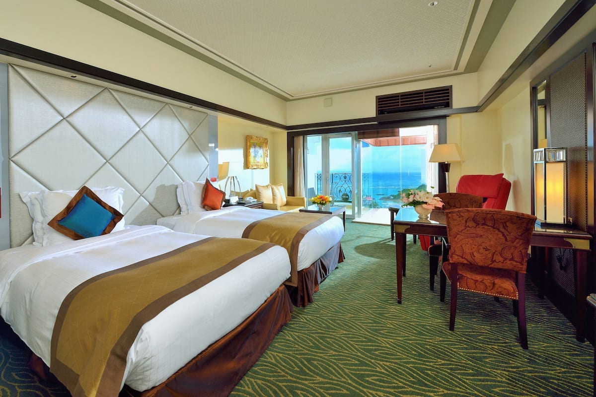Ein Hotelzimmer mit zwei Betten, einem Essbereich und Blick auf den Ozean.