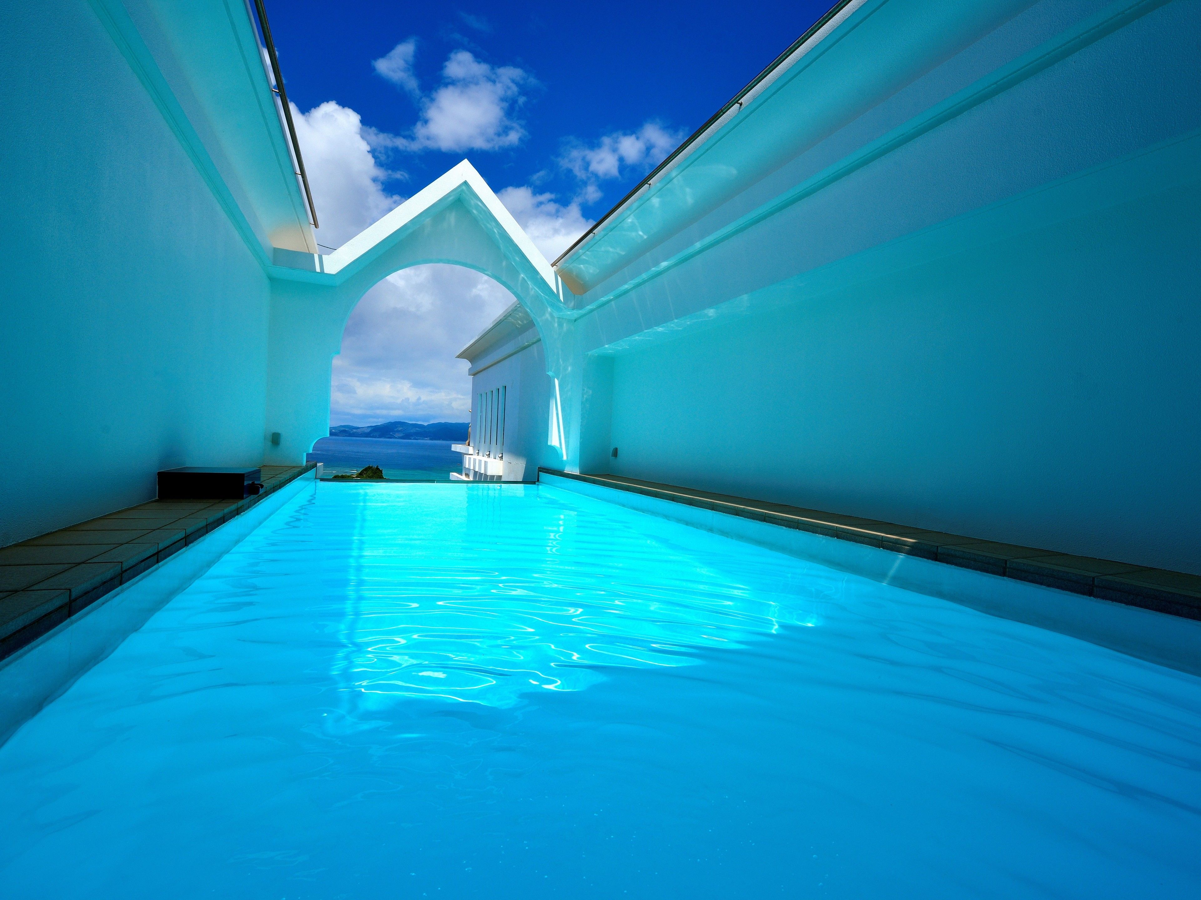 A clear blue pool with a view of the sea and mountains in the background.