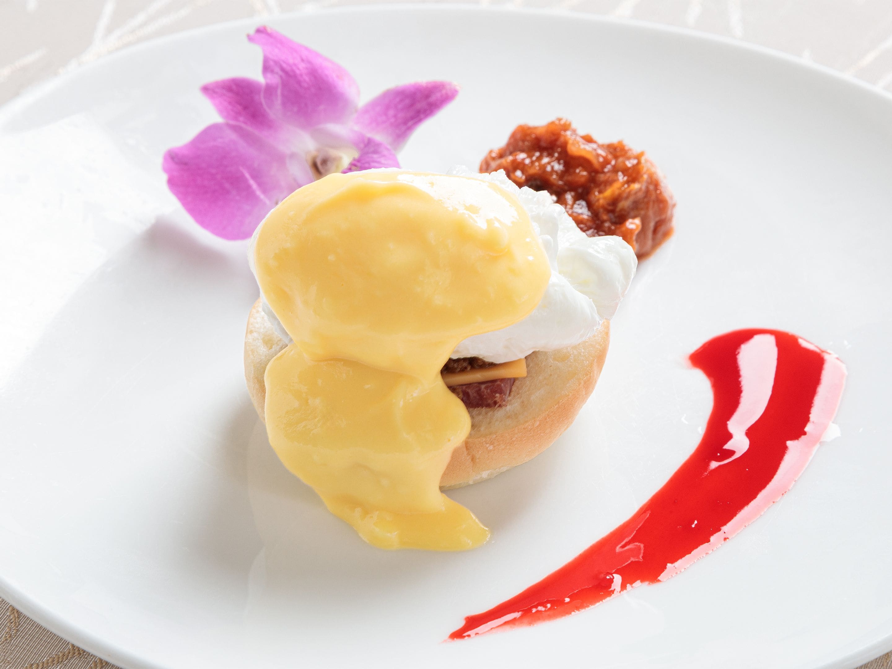 A plate with a sandwich, a dollop of sauce, and a flower.