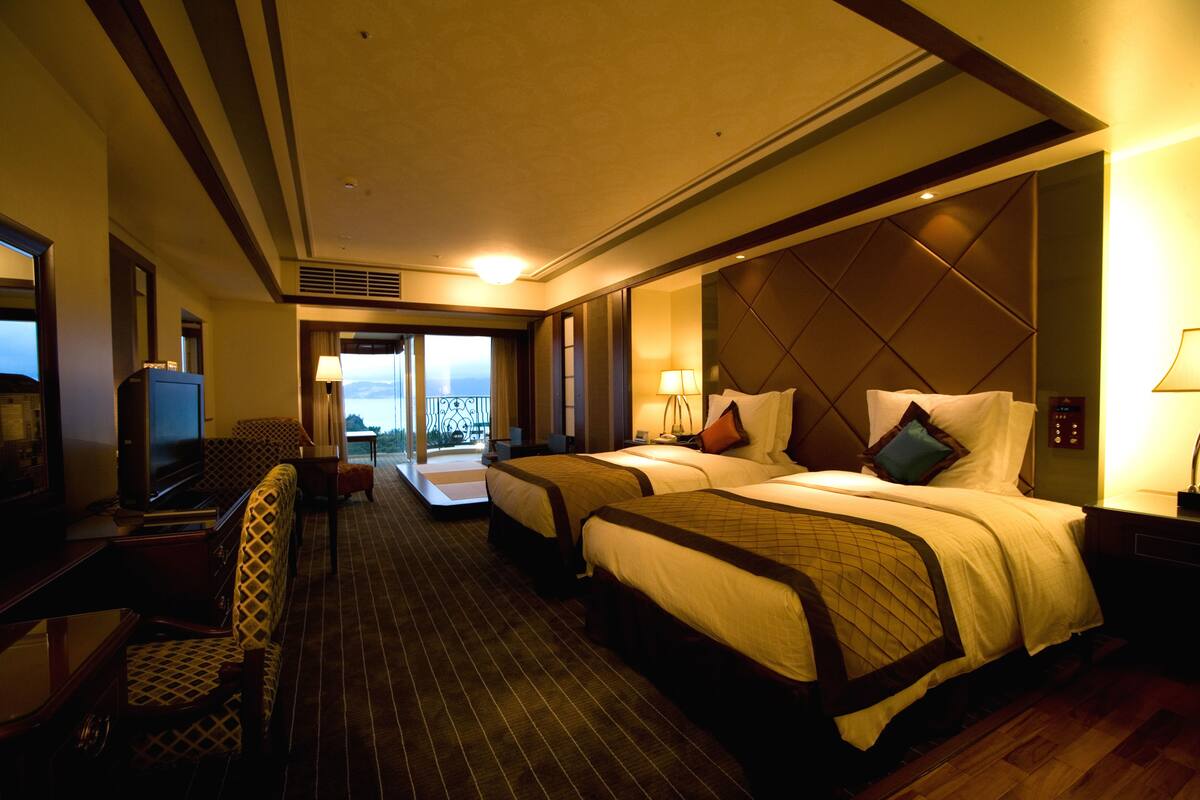 Ein Hotelzimmer mit zwei Betten, einem Fernseher, einem Schreibtisch und Blick auf die Stadt.