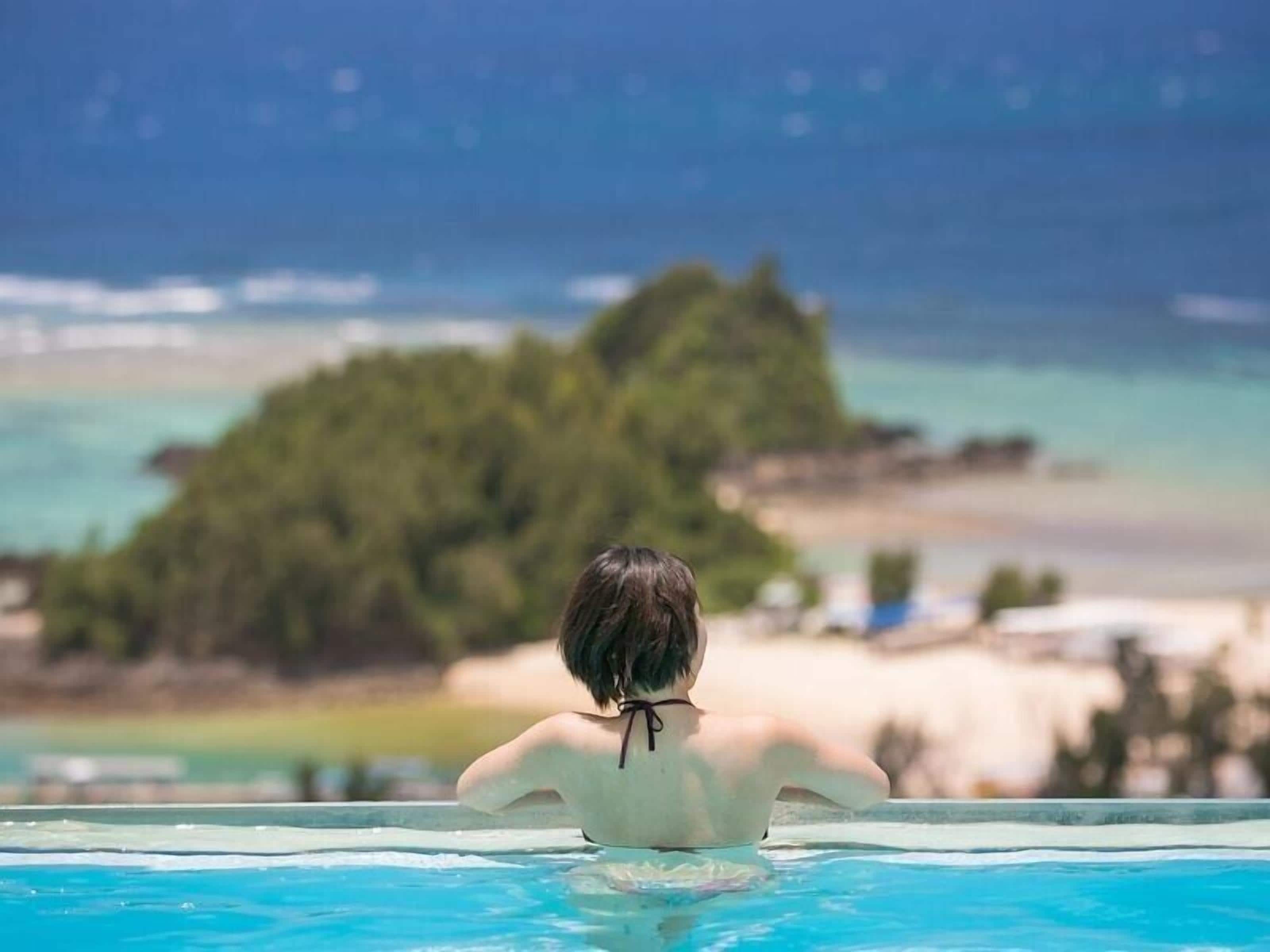 A person in a swimming pool with a view of a beach and a small island.