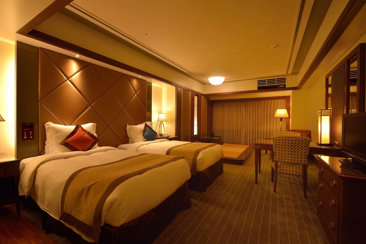 Ein Hotelzimmer mit zwei Betten, einem Fernseher, einem Schreibtisch und einem Sessel.