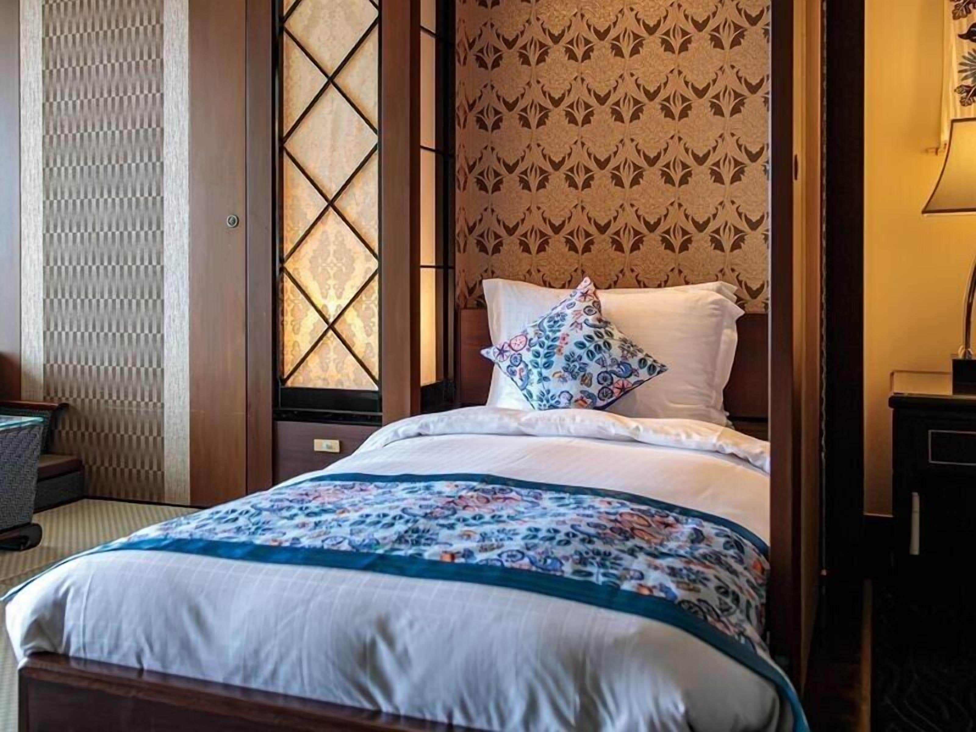 A hotel room with a bed, a patterned wall, and a window with a checkered pattern.