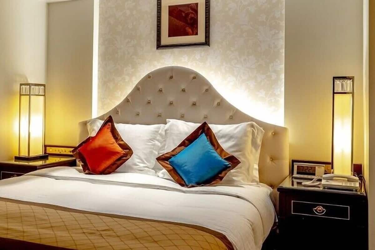 Ein Hotelzimmer mit einem großen Bett, zwei Nachttischlampen, einer Uhr und einem gerahmten Bild an der Wand.