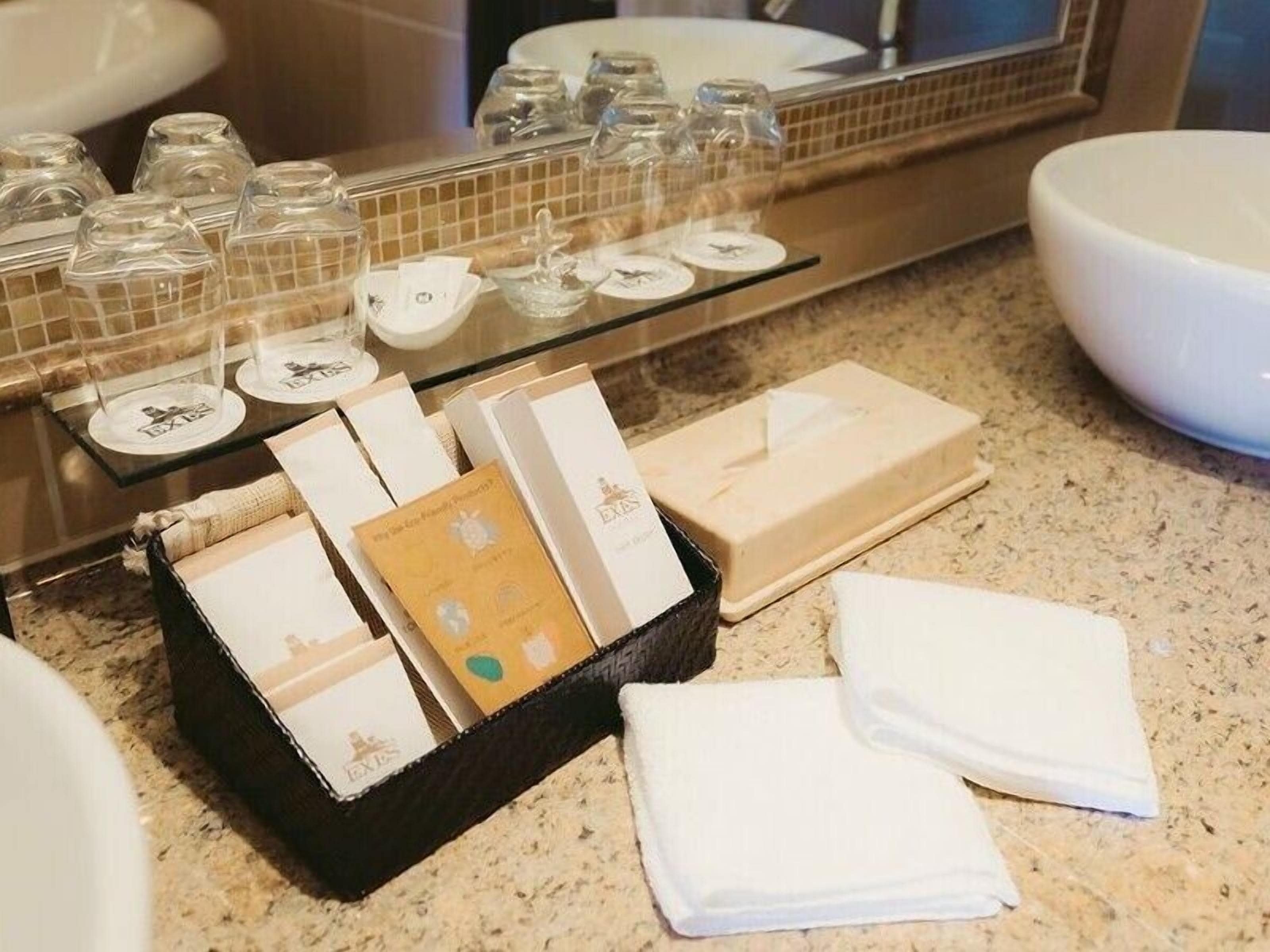 A bathroom with a large mirror, a sink, and various toiletries including a black toiletry bag, a white towel, and a soap dish.