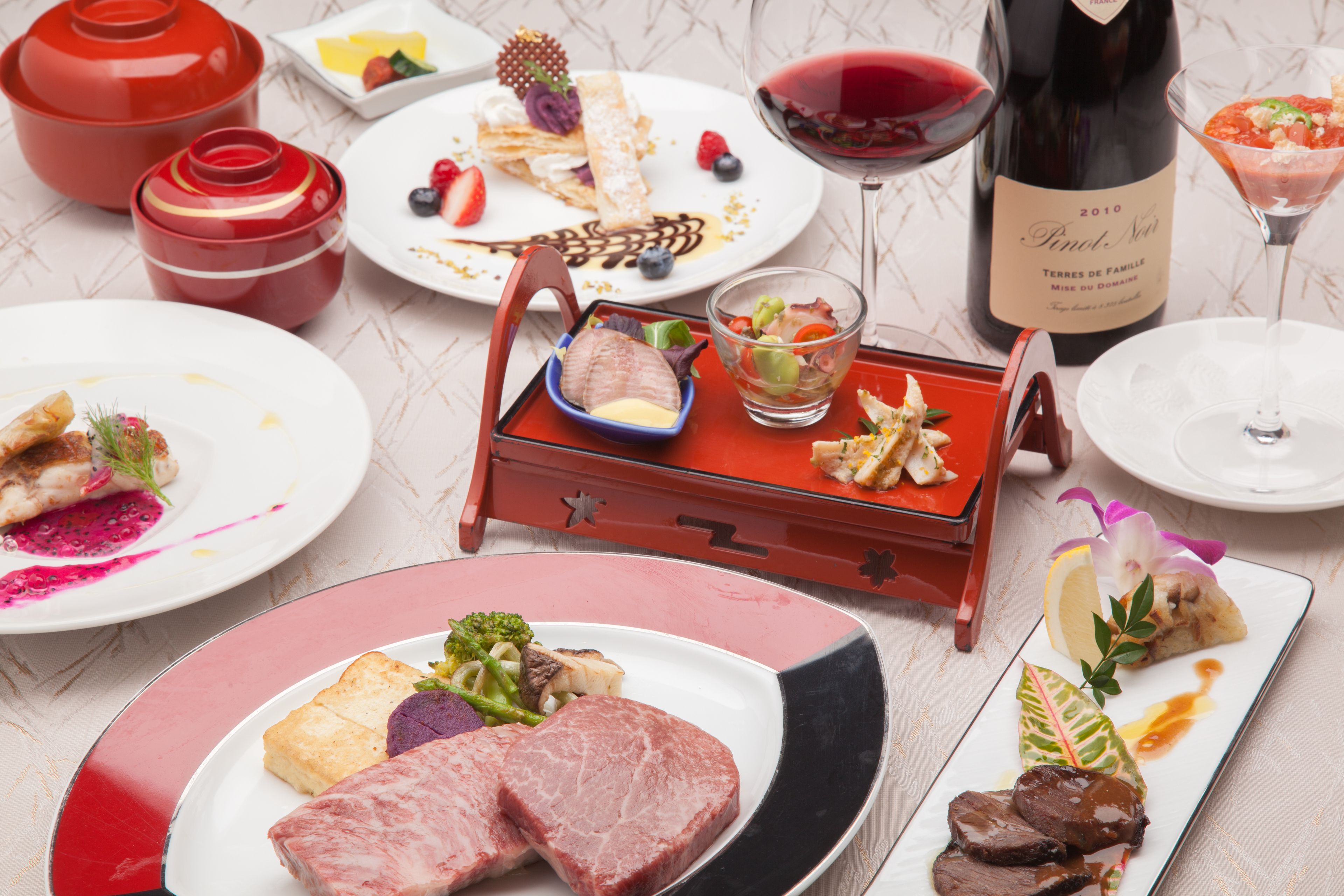 Una variedad de platos, como carne, mariscos y postres, junto con botellas y copas de vino.