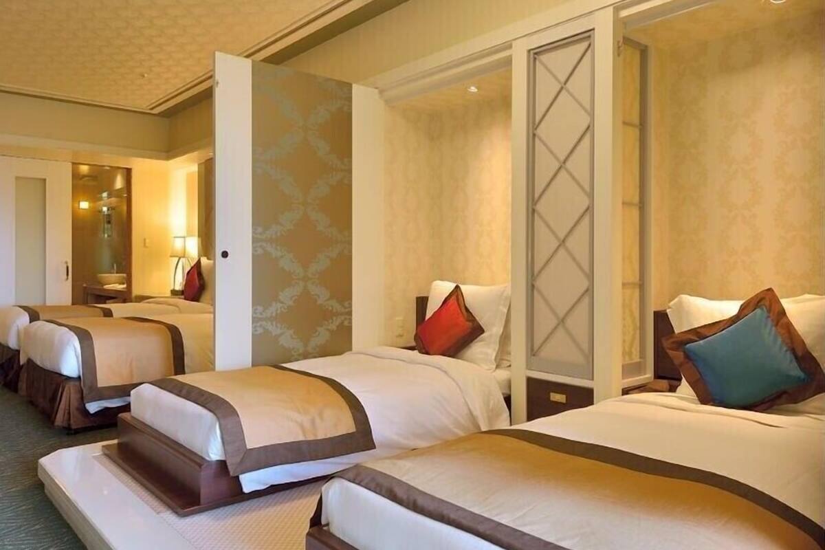 Ein Hotelzimmer mit drei Betten, jeweils mit brauner Kopfteil, weißer Bettwäsche und Zierkissen.