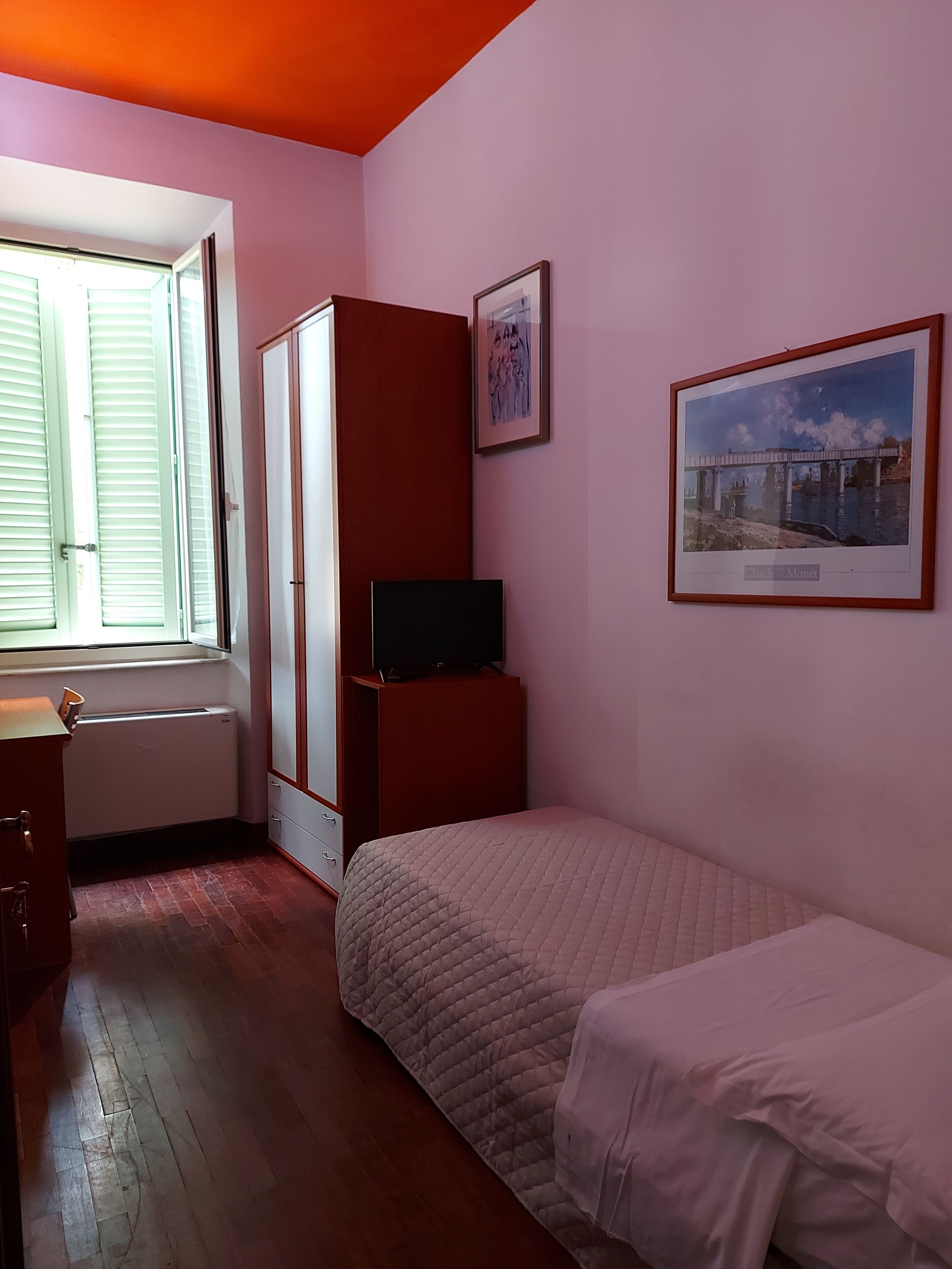 Un dormitorio con cama, televisor sobre un mueble, armario y ventana.