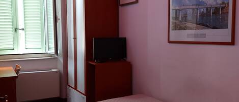 Un dormitorio con cama, televisor sobre un mueble, armario y ventana.