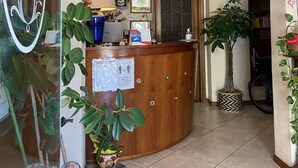 Zona de recepción con mostrador de madera, cuadros en la pared, una planta en maceta y un letrero que indica medidas de distanciamiento social.