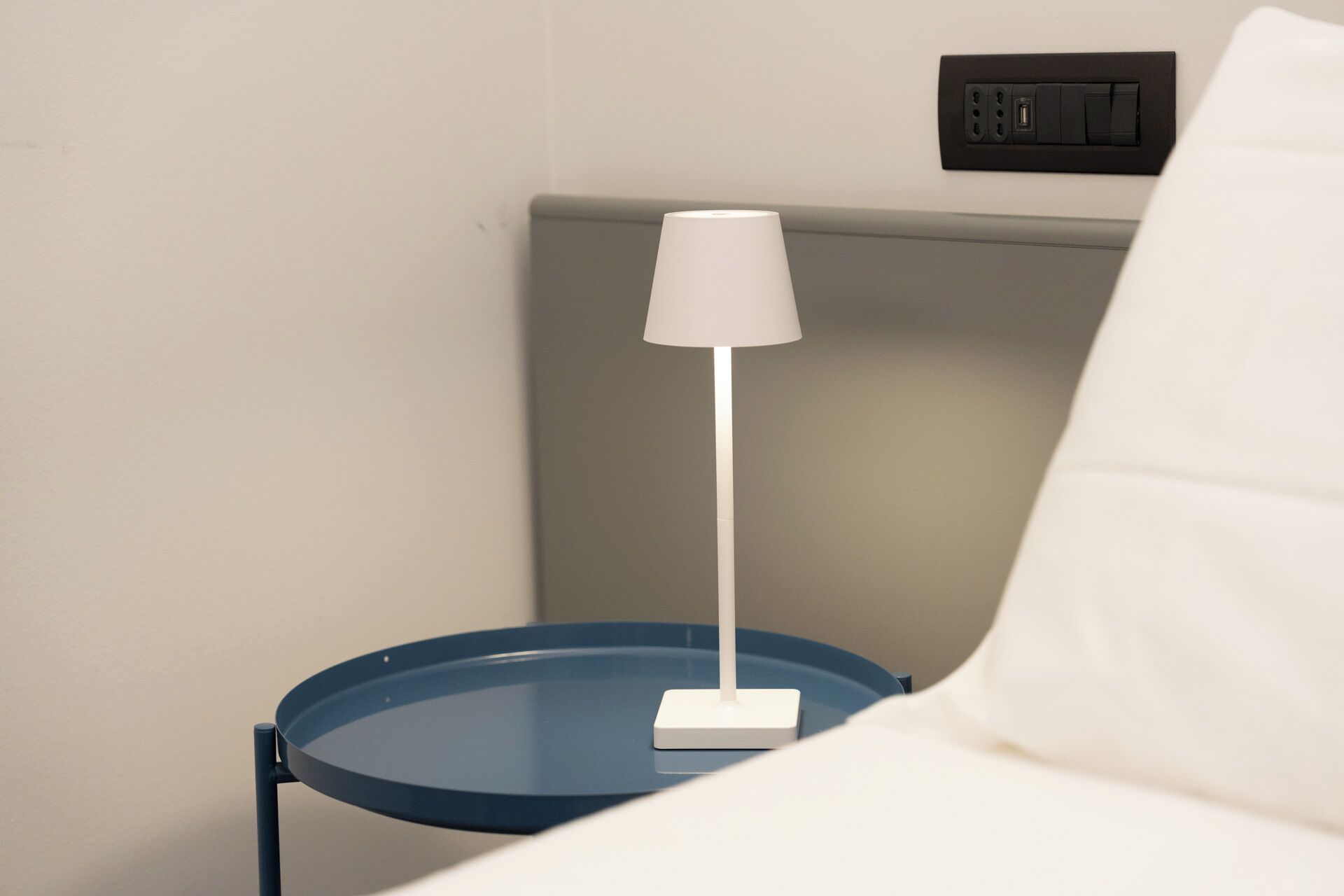 Una lampada bianca su un tavolino azzurro accanto a un divano bianco.