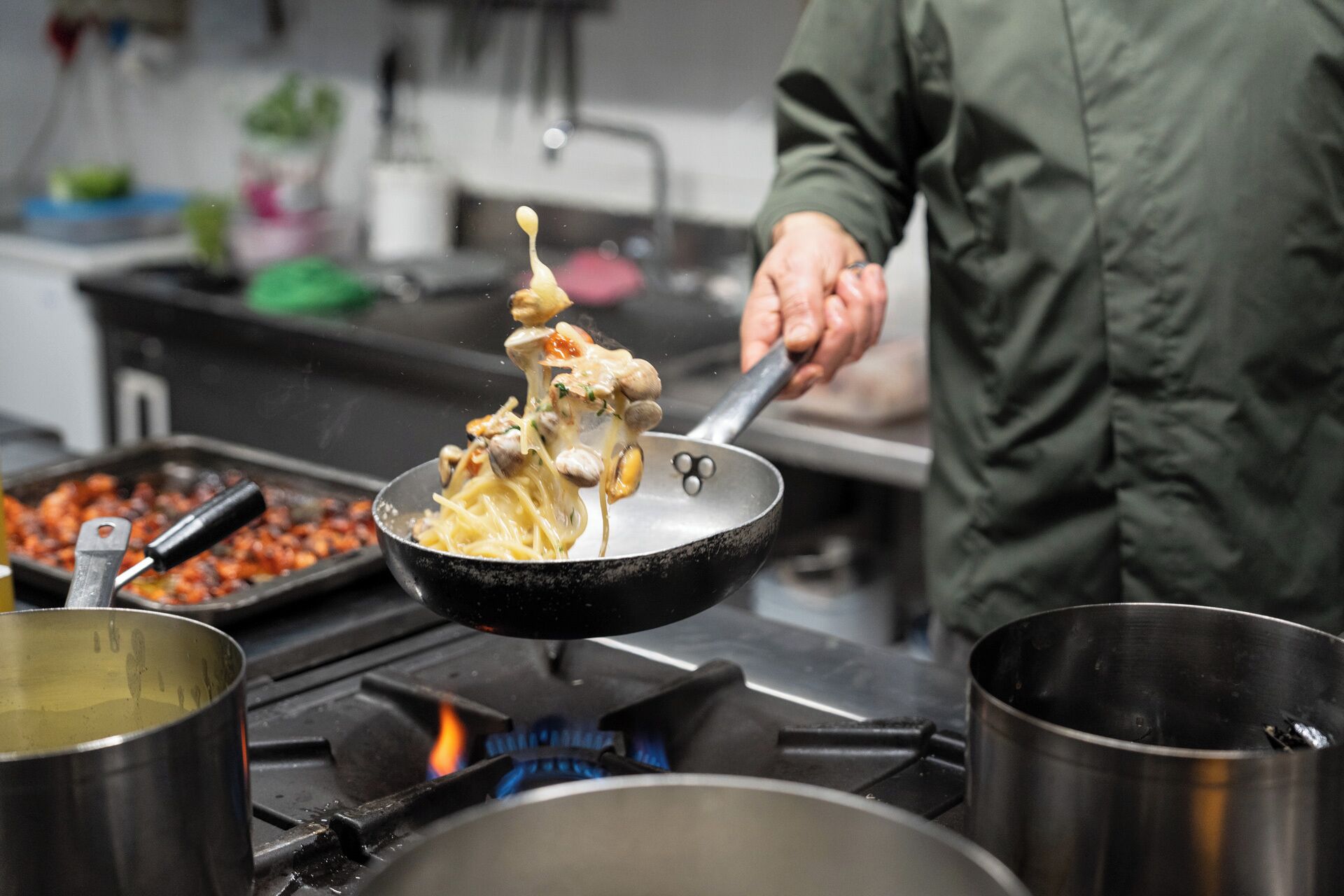 A person cooking noodles in a pan on a stove.