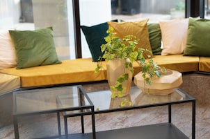 Uma sala de estar moderna com uma mesa de centro de vidro, um sofá com almofadas e um vaso de planta.