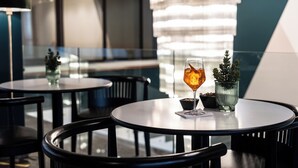 A modern dining area with round tables, chairs, and a glass of amber-colored beverage. - Cristal Palace Hotel (Andria)