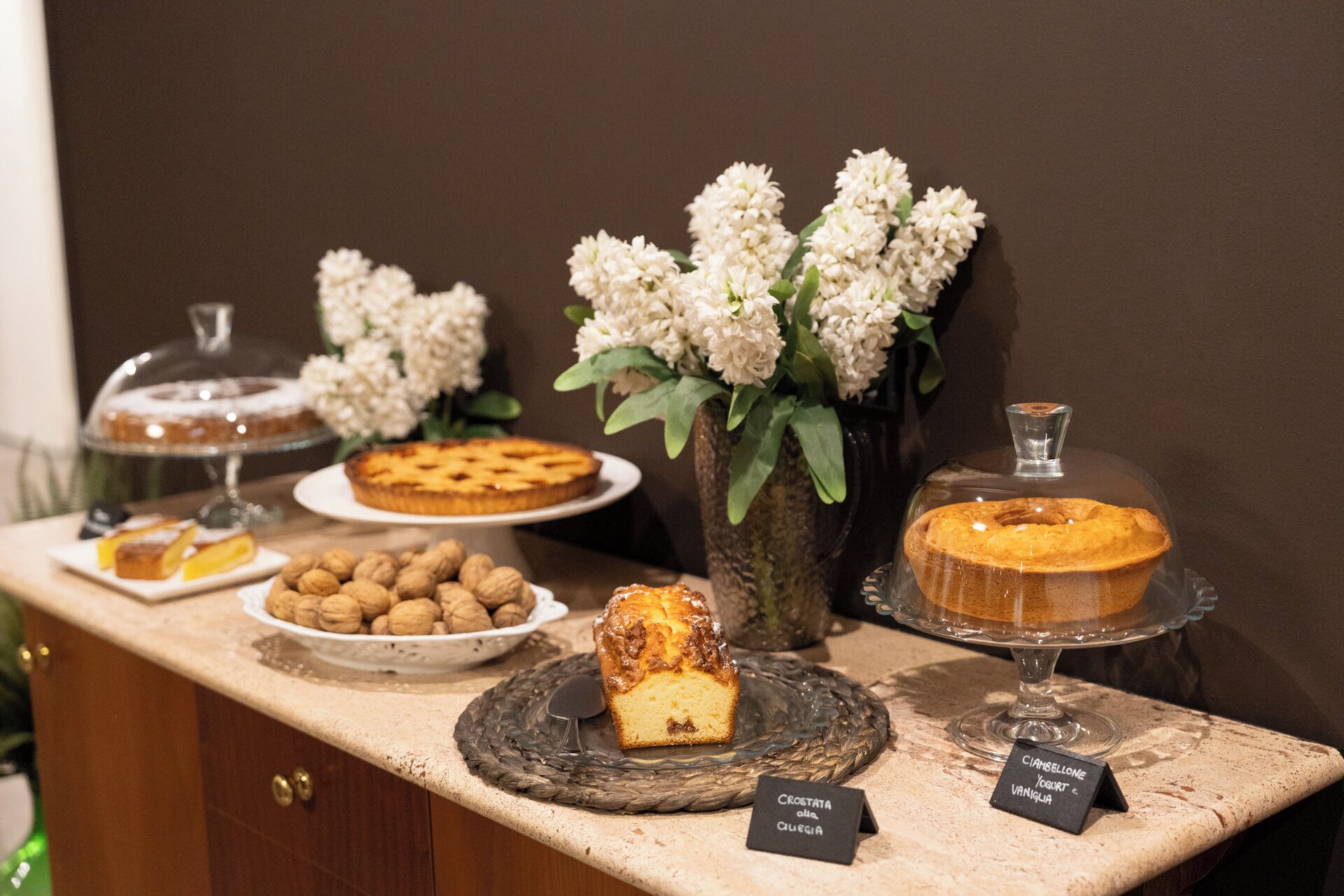A dessert display with various cakes and pastries, including a Crostata, a Cianella, and a Cianella with yogurt and vanilla.