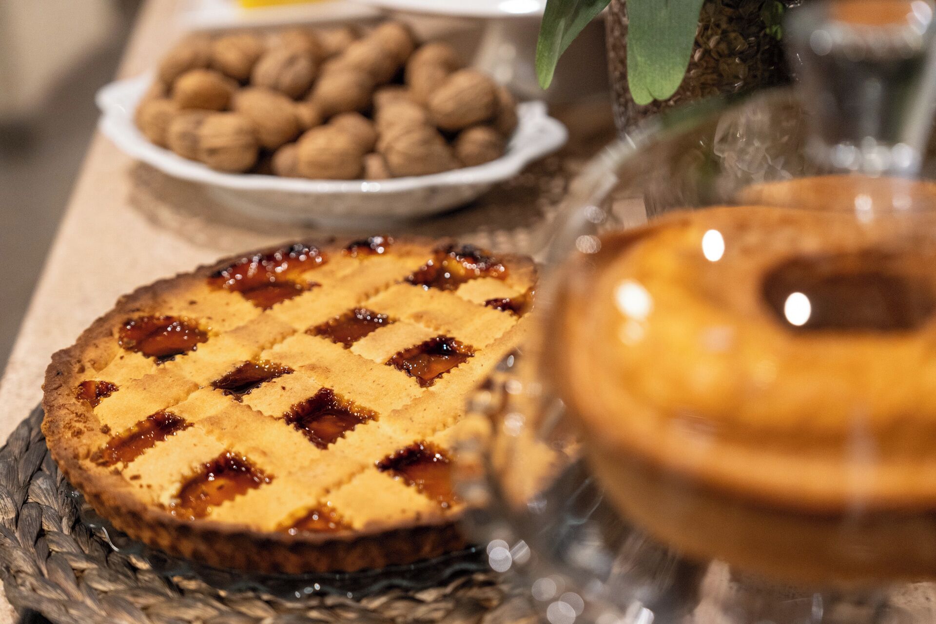 Tarta con corteza de rejilla sobre un plato de vidrio, un cuenco de nueces y un recipiente de vidrio con tapa.