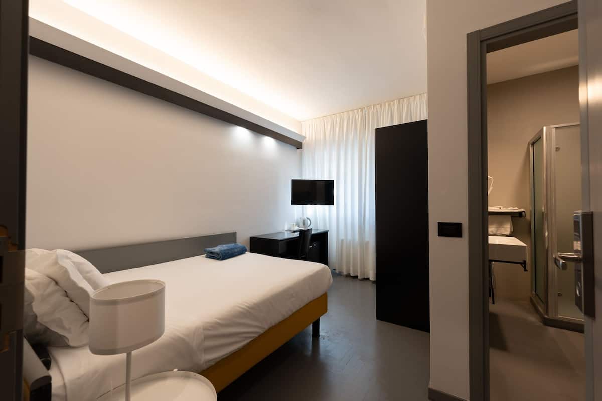 A modern hotel room with a bed, bedside table, lamp, and a television.
