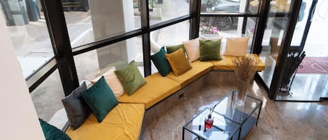 Un interior moderno con un sofá curvo, una mesa de centro de vidrio y ventanas amplias que ofrecen vistas a la calle.