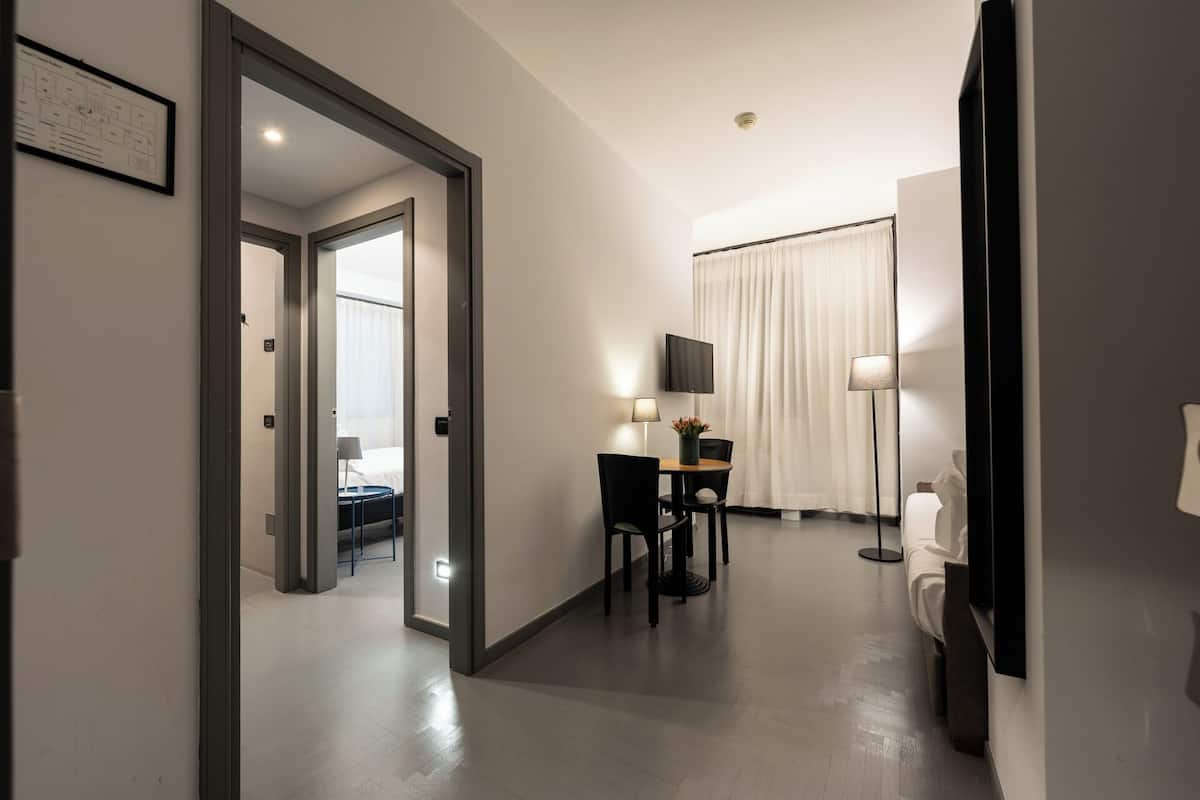 A hotel room with a bed, a desk with a chair, a TV, and a lamp.
