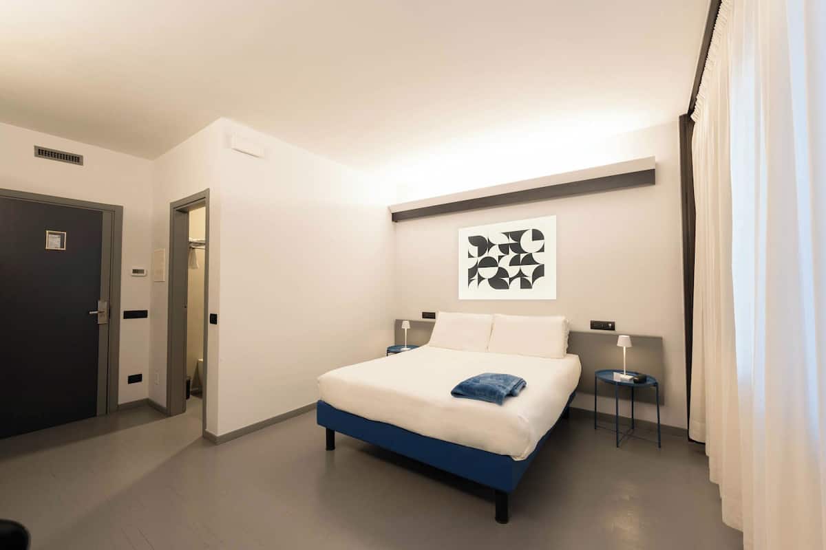 A hotel room with a bed, bedside tables, a wall-mounted artwork, and a door.
