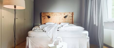 A bedroom with a wooden headboard, white bedding, a standing lamp, and a fur rug.
