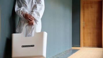 A person holding a white MIRAMONTE tote bag, standing in a hallway with a wooden door and a blue wall.