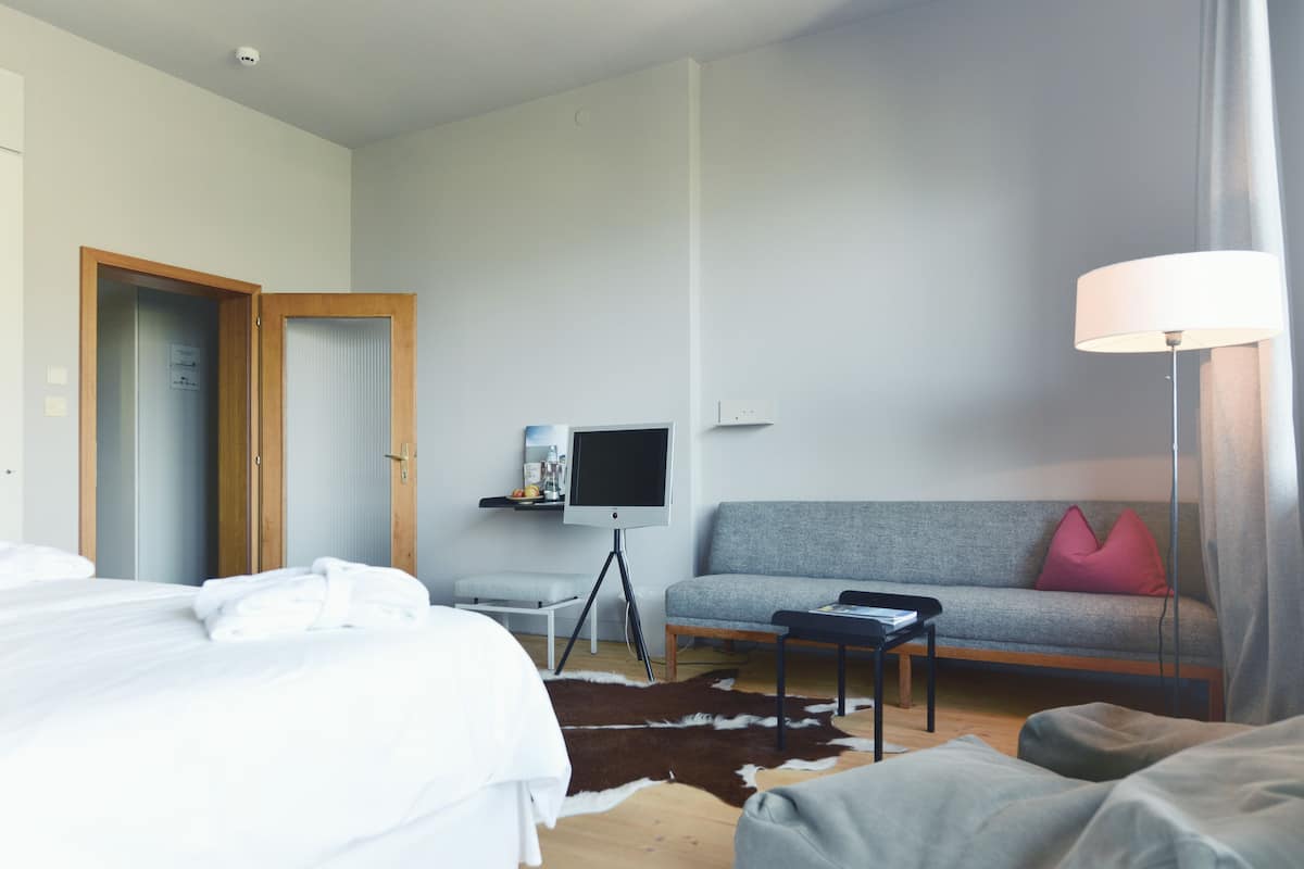 A hotel room with a bed, a sofa, a TV, and a lamp.