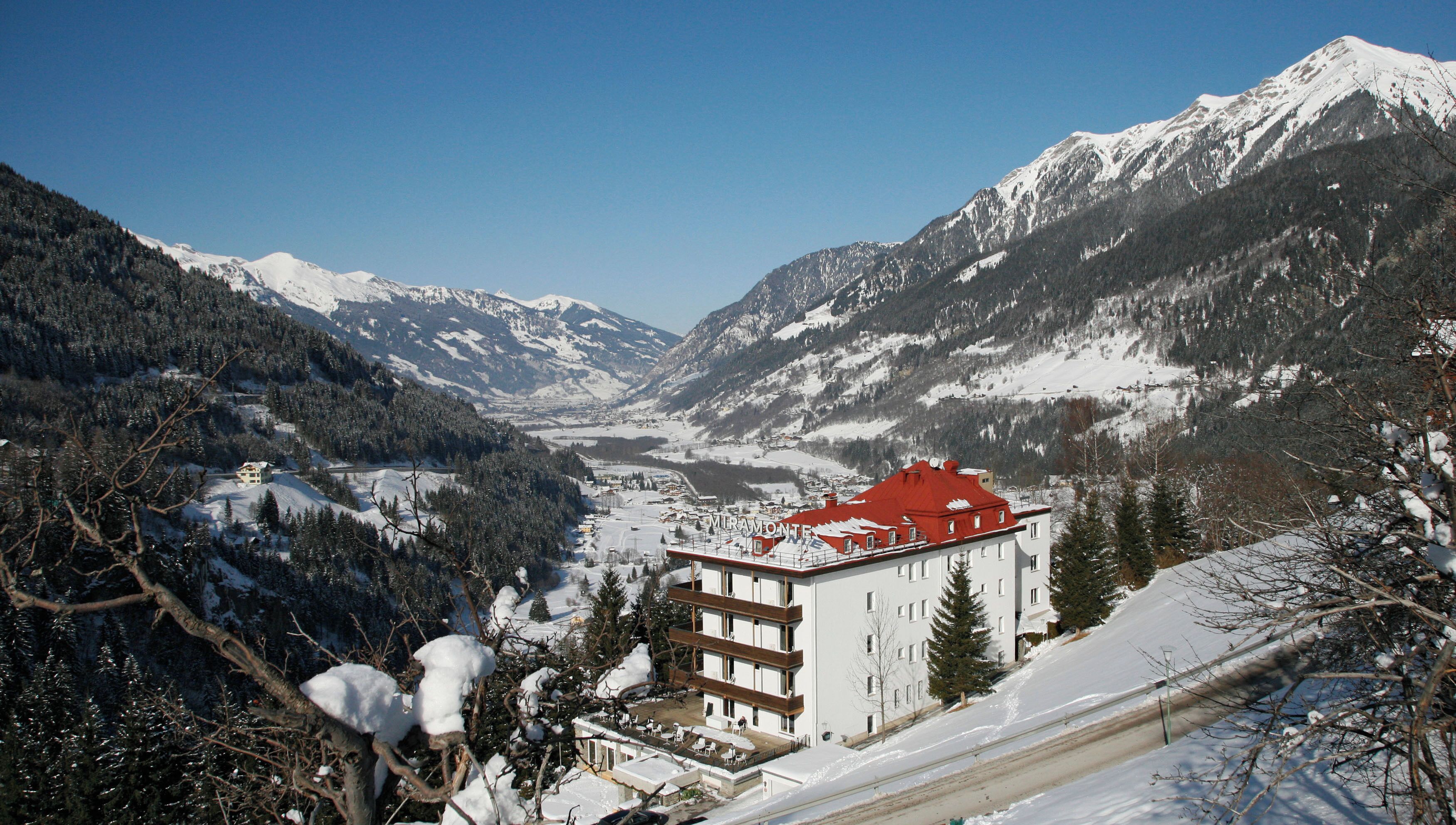 Un hotel con techo rojo, rodeado de montañas y árboles cubiertos de nieve.