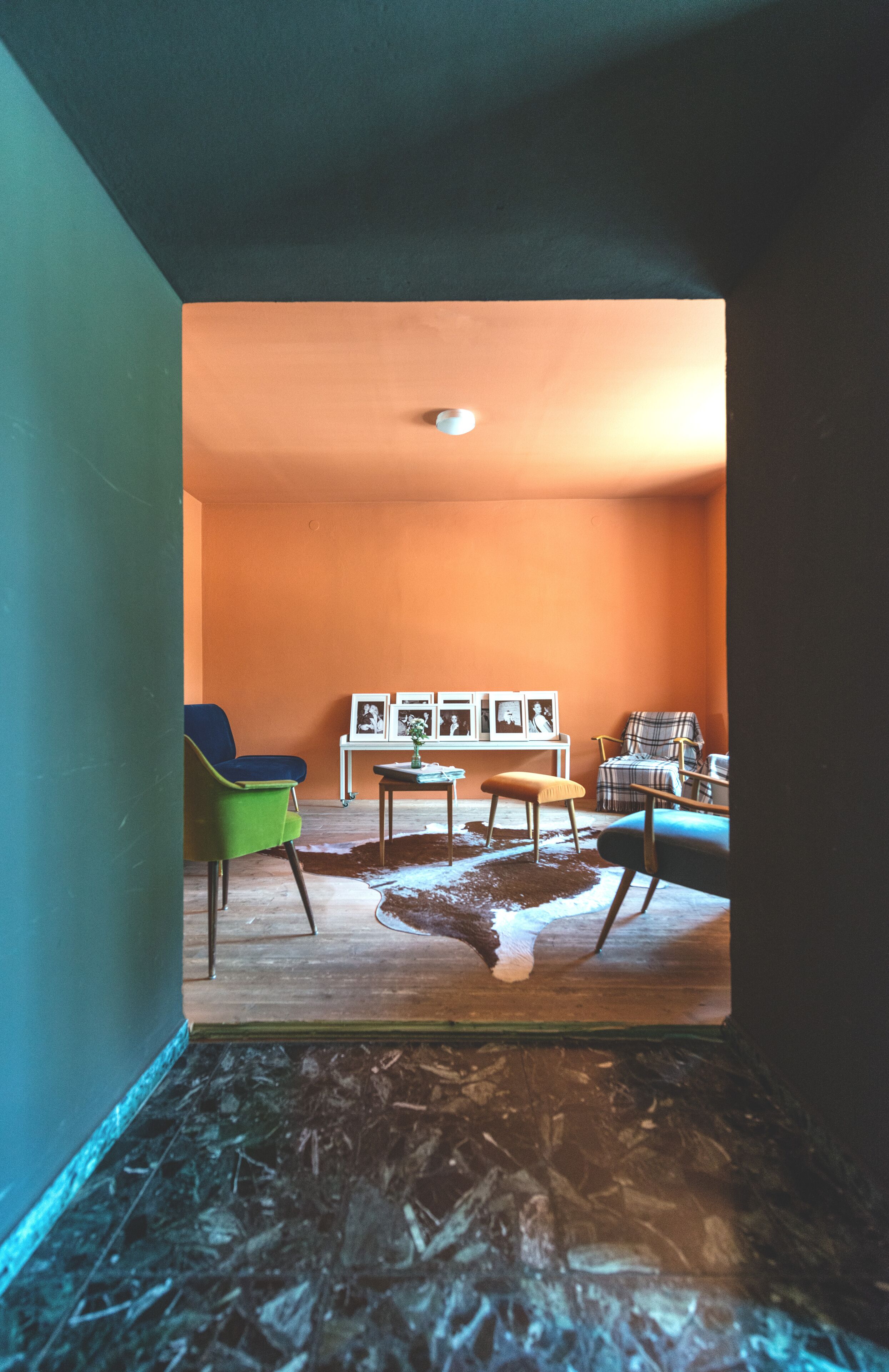 A room with a green chair, a plaid chair, a small table with pictures, and a cowhide rug.