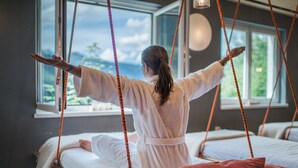 A person in a white robe sitting on a bed with a view of the outdoors through a window. - Miramonte (Bad Gastein)
