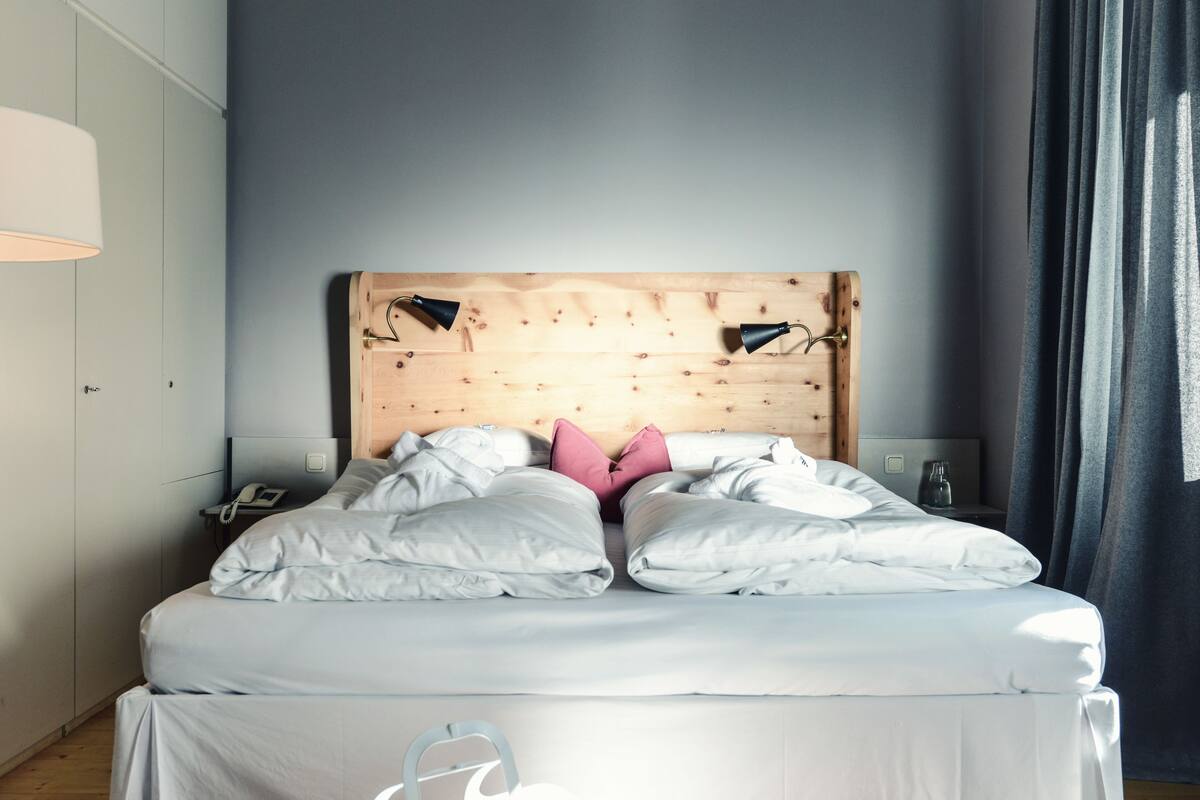 A bed with a wooden headboard, white bedding, and a pink pillow.