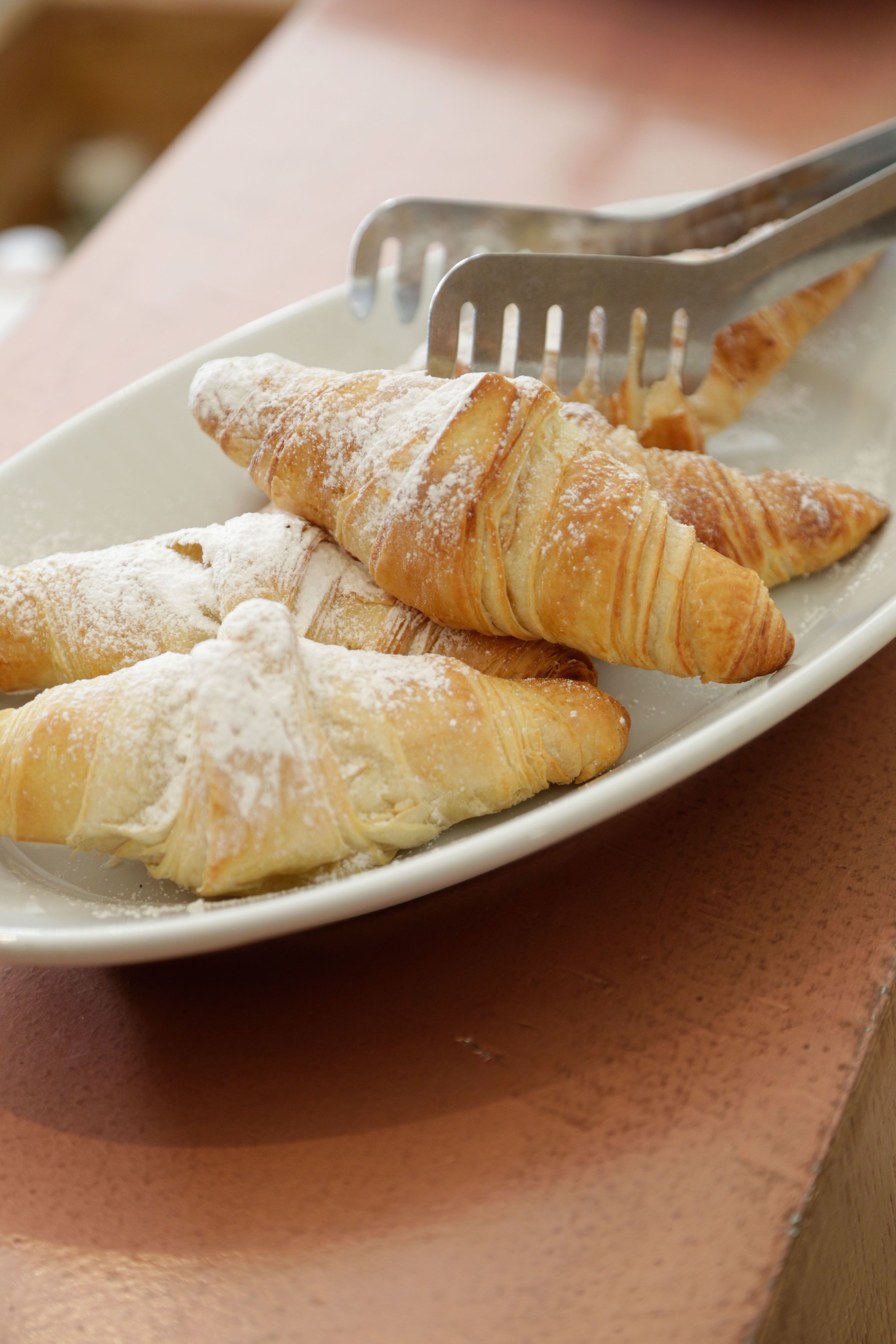 A plate with three croissants dusted with powdered sugar, accompanied by a fork.