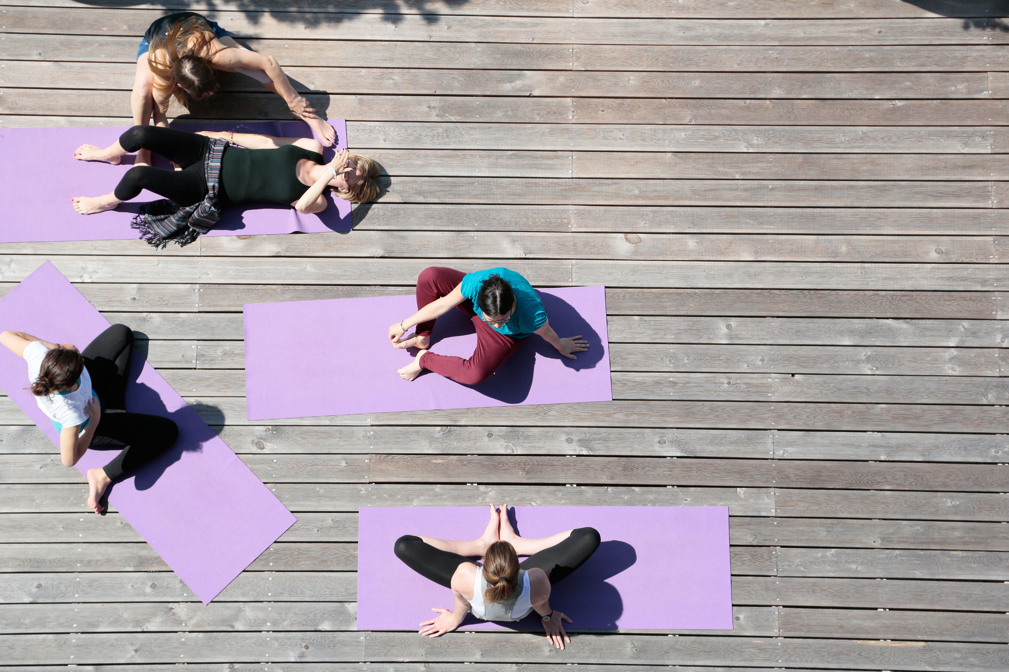Un groupe de personnes, sur des tapis de yoga violets, pratiquent des exercices sur une terrasse en bois.