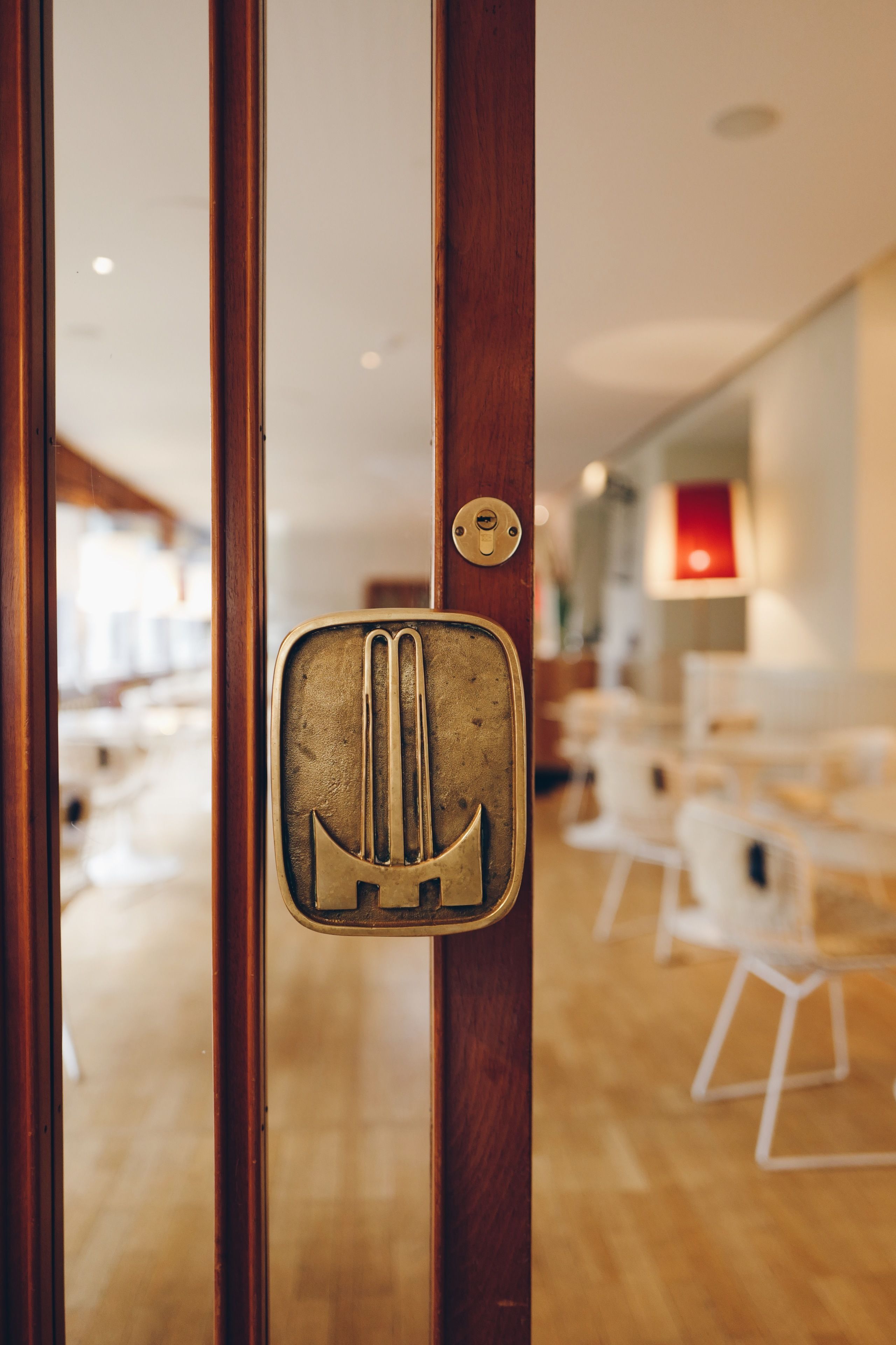 A door with a brass handle and a keyhole, leading to a room with white chairs and a wooden floor.