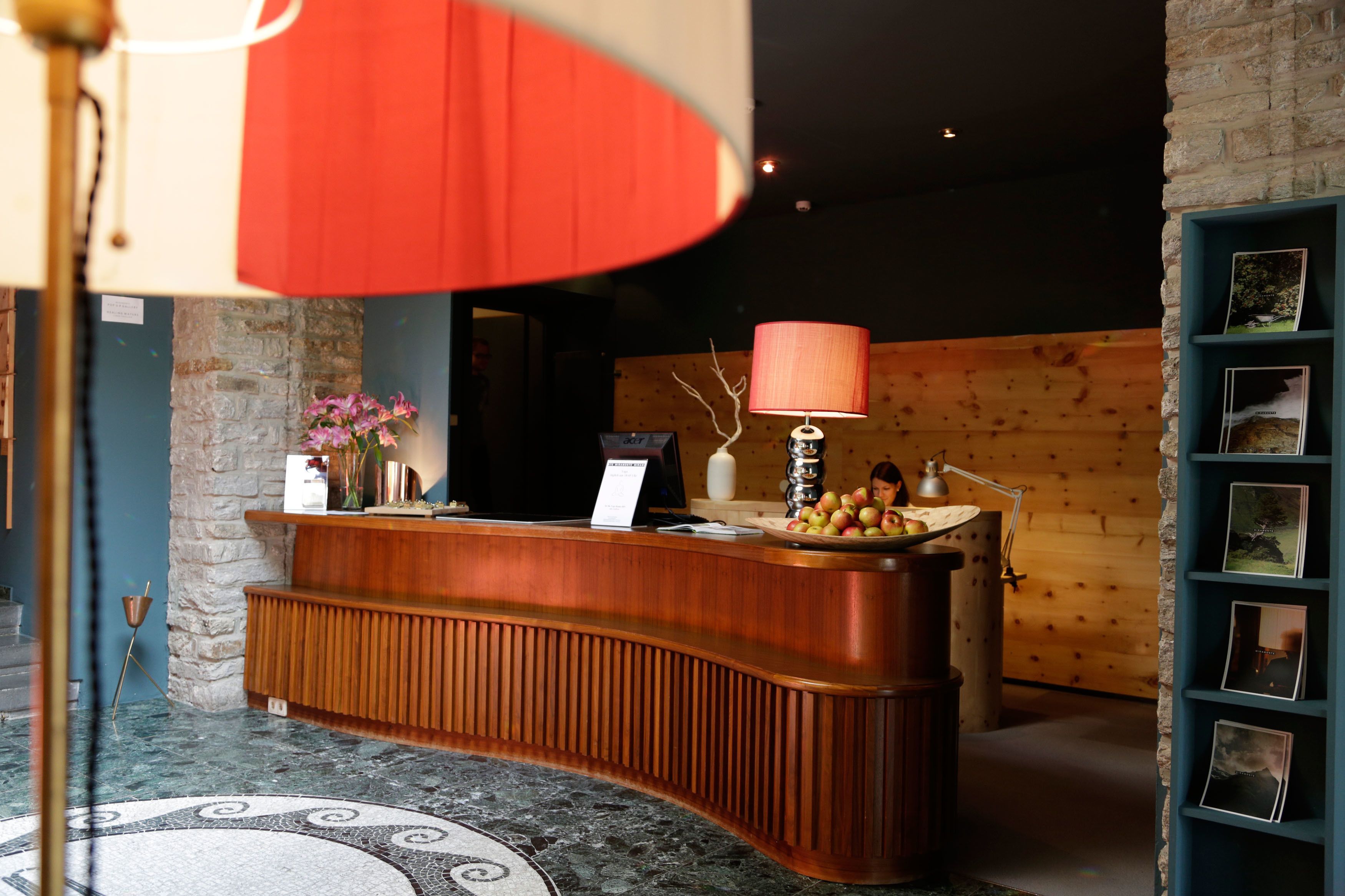 A reception desk with a wooden finish, a red lamp, and a small vase with flowers.