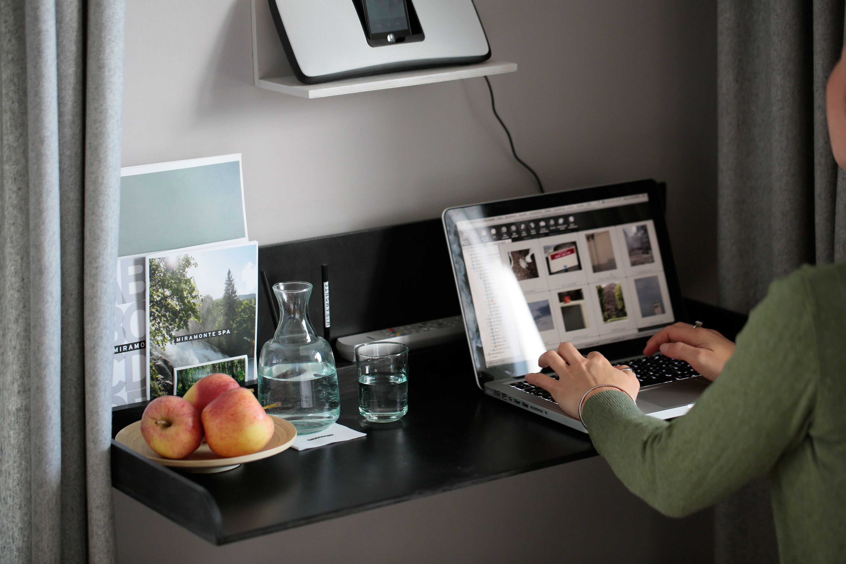 A laptop on a desk with a plate of apples, a glass of water, and a bottle.