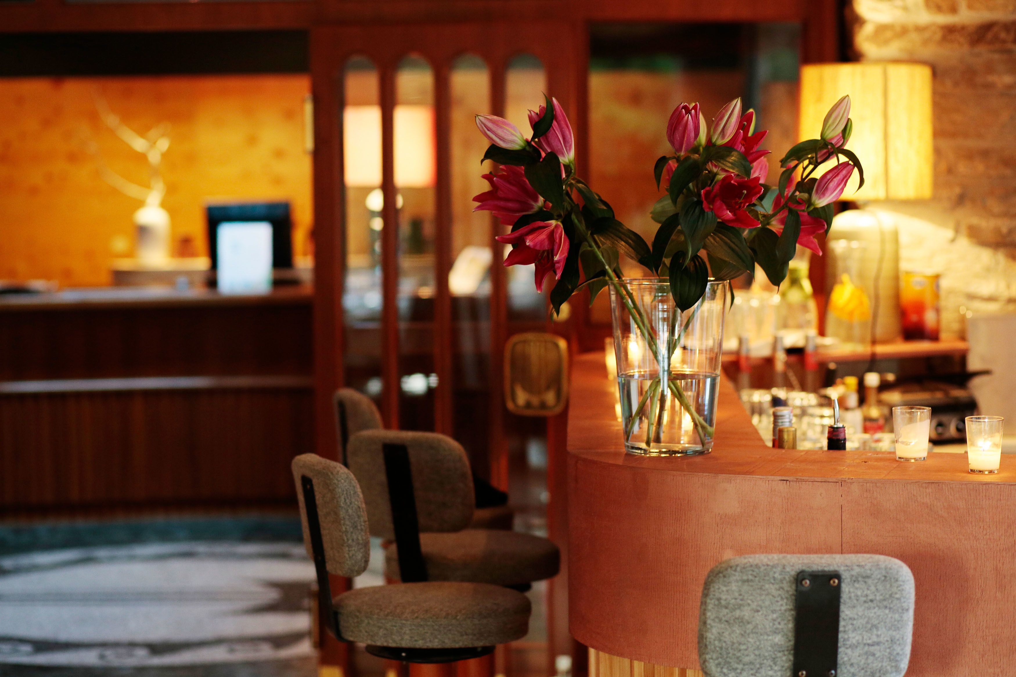 Una zona de bar con mostrador de madera, sillas y un jarrón con flores.