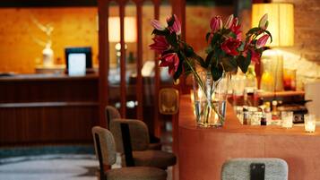A bar area with a wooden counter, chairs, and a vase with flowers.