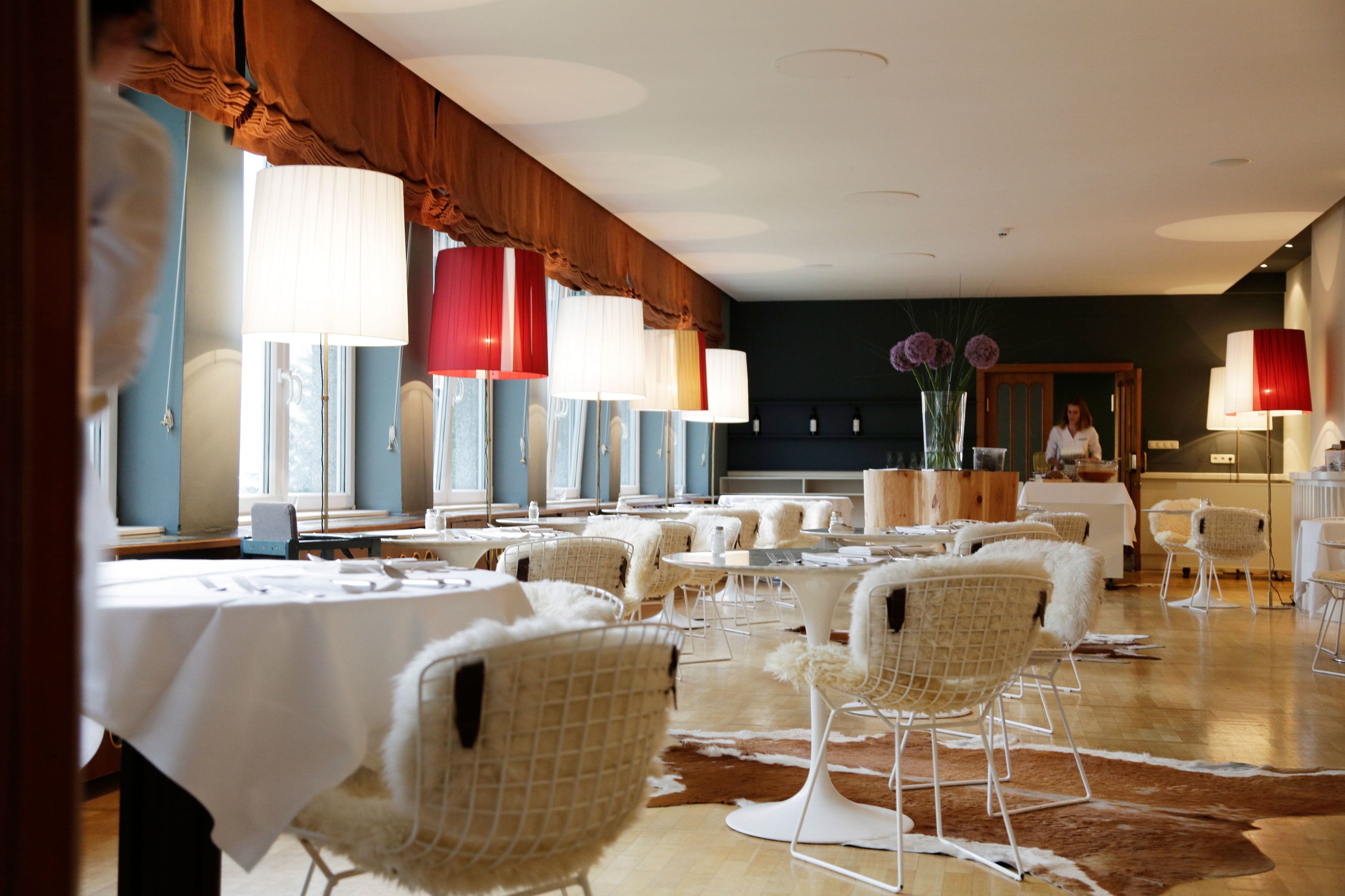 Un vaste espace dédié à la salle à manger, avec plusieurs tables et chaises, de grandes fenêtres et un tapis en peau de vache sur le sol.