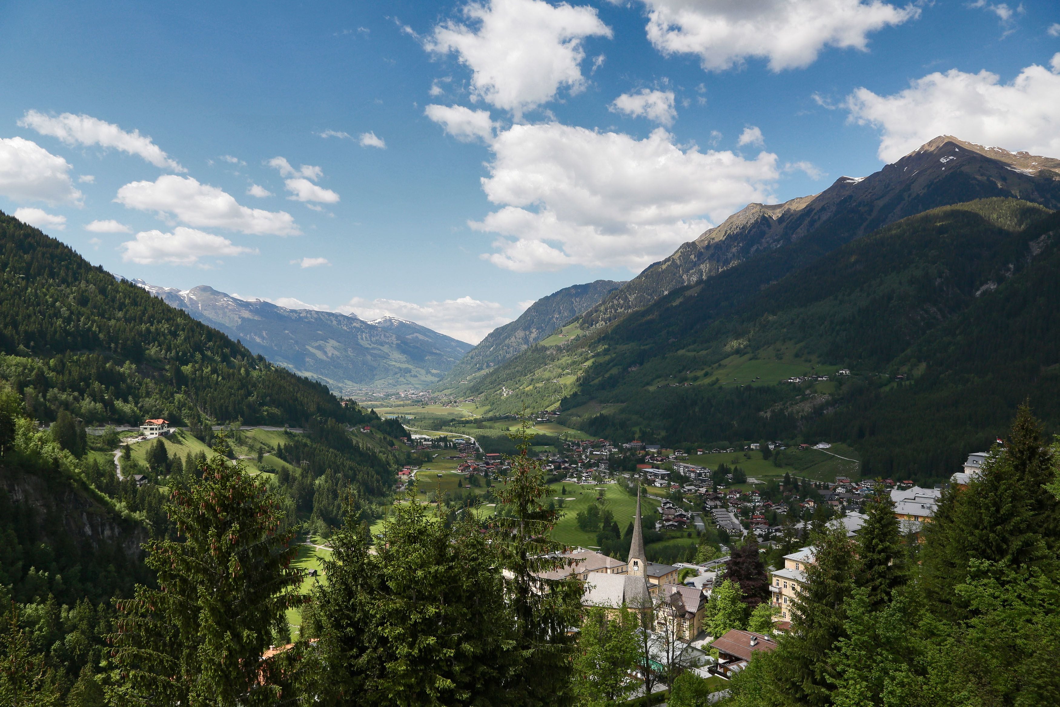 Un paysage montagneux avec une ville nichée dans une vallée, entourée d’une végétation luxuriante et dominée par le clocher imposant d’une église.