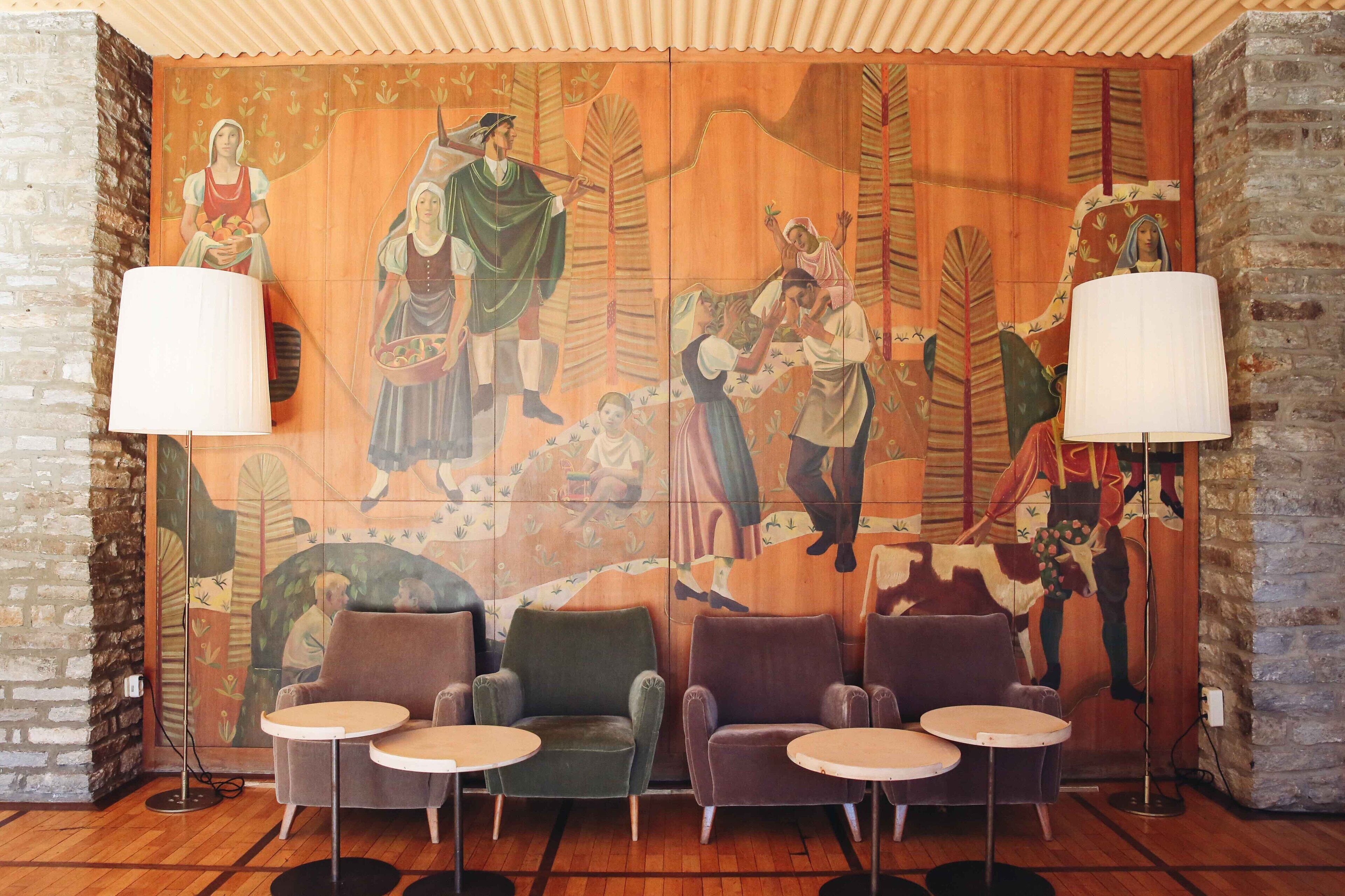 A room with a mural, four armchairs, and two small tables.