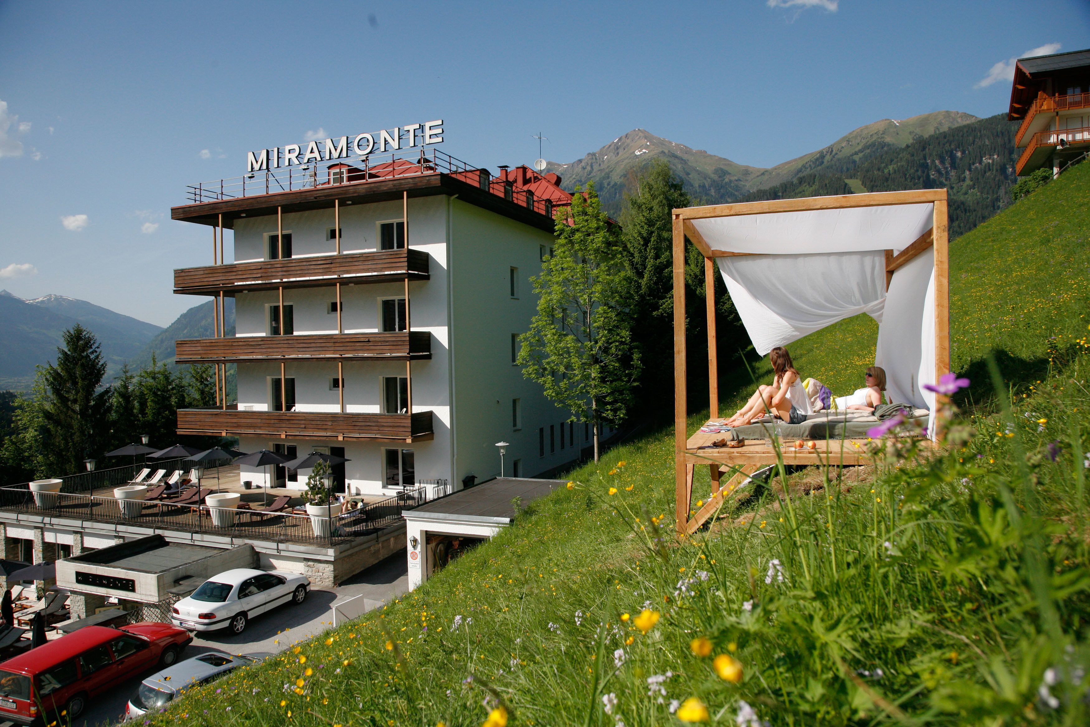 Hotel MIRAMONTE met een balkon, een auto ervoor en een bed op een grasheuvel.