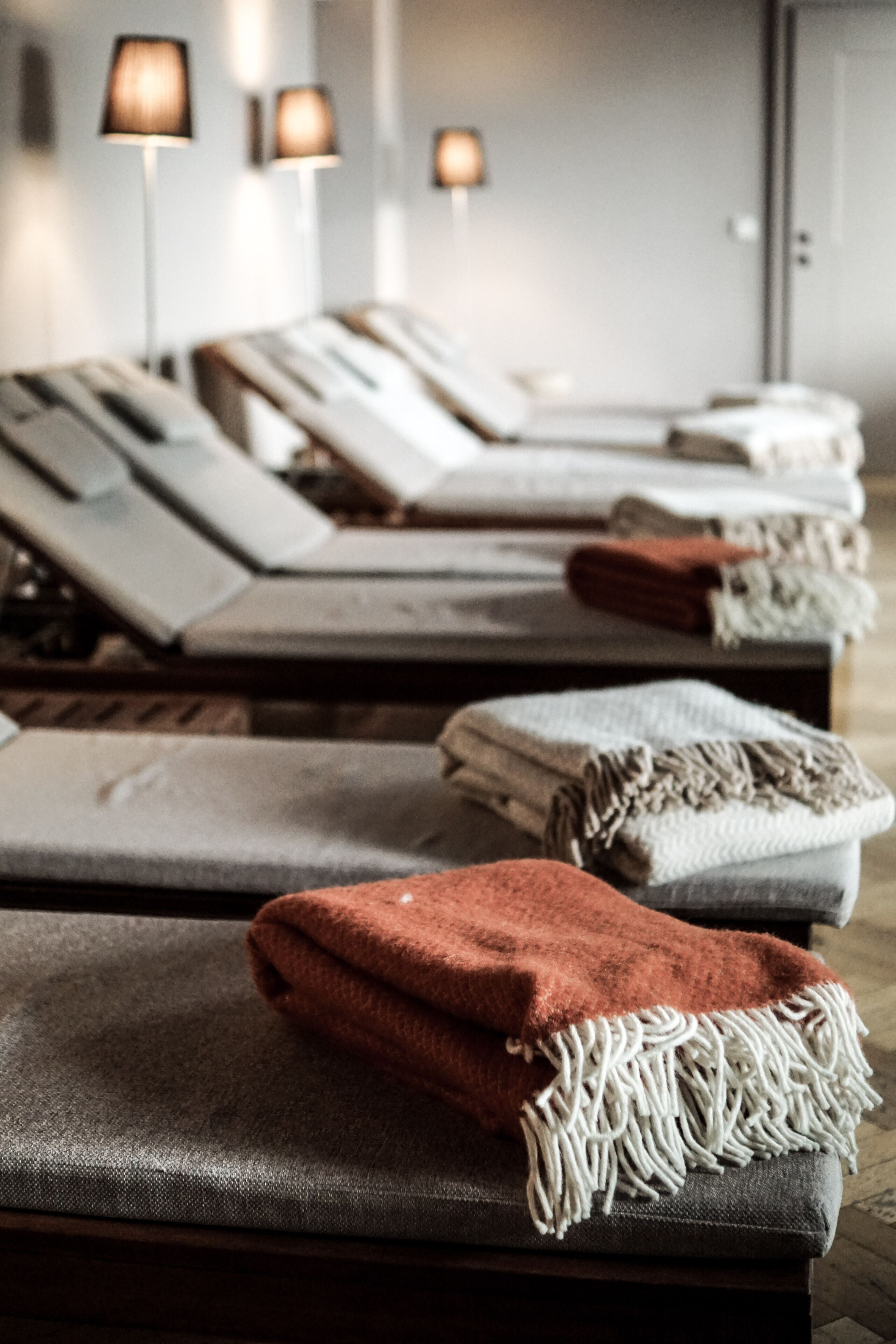 A room with multiple beds, each with a blanket and a lamp.