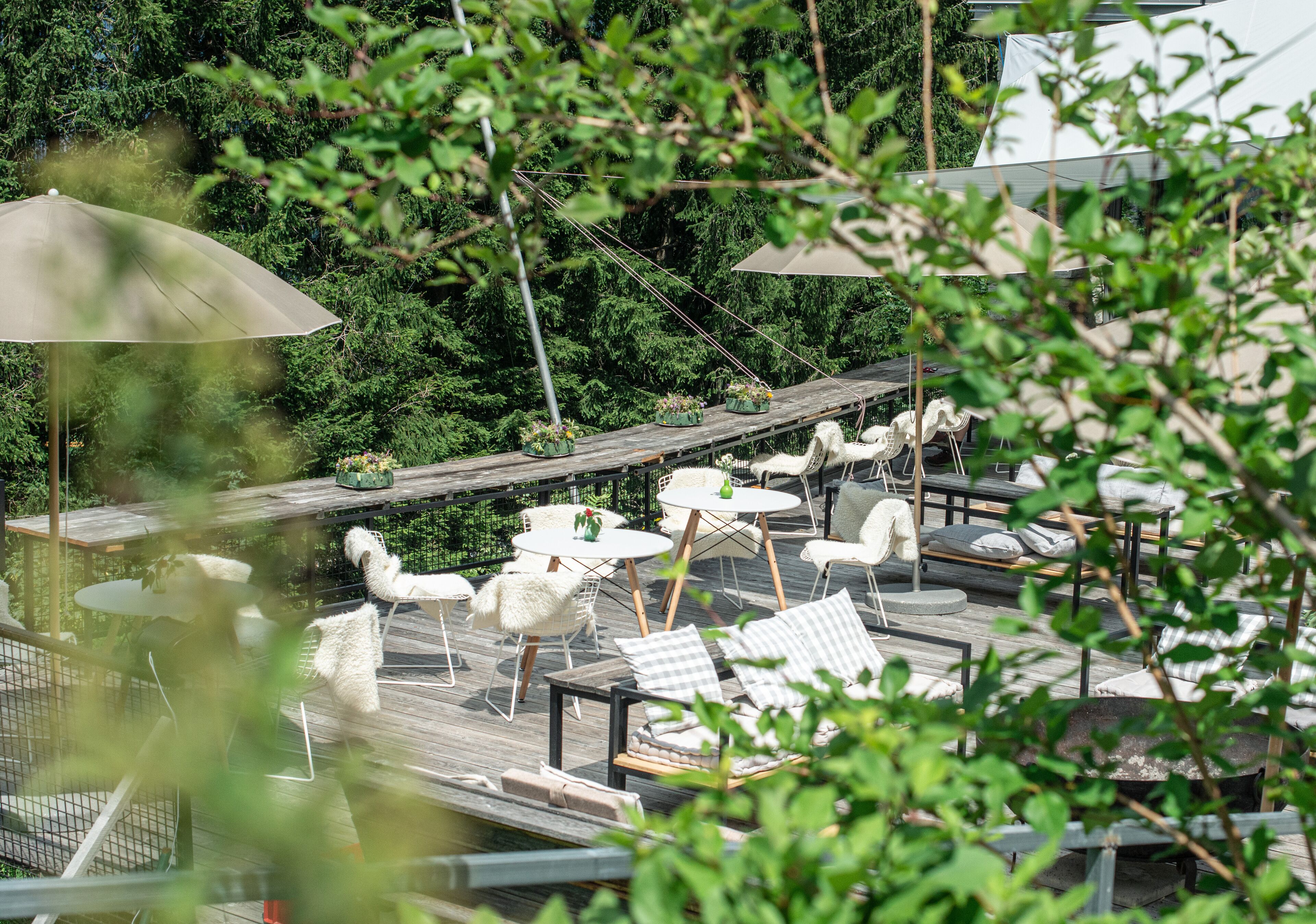 Une terrasse sur le toit, avec des chaises et des tables blanches, entourée d’une végétation luxuriante.