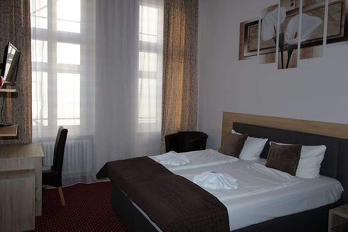 A hotel room with a large bed, a desk, and a chair. There are curtains on the windows and a painting on the wall.