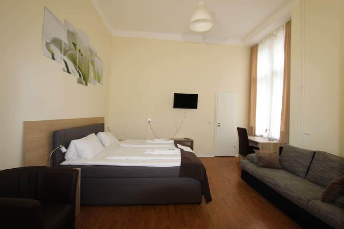 A hotel room with a bed, a sofa, a TV, and a desk.