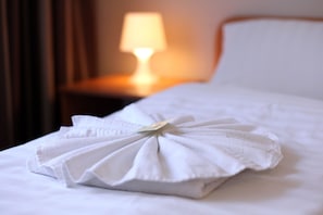 A neatly made bed with a folded white towel placed on it.